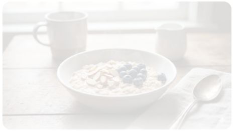 이미지 추천: 따뜻한 김이 모락모락 나는 오트밀 죽 위에 아몬드 슬라이스와 블루베리가 몇 알 올라가 있는 정갈한 아침 식사 풍경